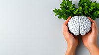 Hands holding white brain model with green parsley leaves above on light background. Mental health, neurology and brain function concept for medical design.