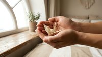 Young woman hands holding small green plant sprout in cupped palms by sunny window, symbolizing growth, care, new life and environmental protection.