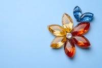 Colorful crystal flower made of amber, red and blue gemstones with diamond center on light blue background. Jewelry design element on pastel surface.