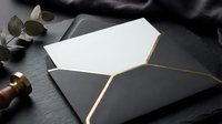 Elegant black envelope with gold foil lining and white card on dark slate surface with eucalyptus branch for luxury wedding invitations and stationery.