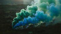 Vibrant blue and green smoke clouds billowing dramatically against dark landscape creating atmospheric special effects for creative projects.