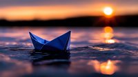Blue paper boat floating on water surface at sunset with sun reflection creating magical atmosphere and rippling waves in orange and purple hues.