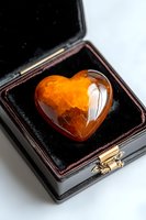 Orange polished citrine heart crystal in black velvet jewelry box on white background, natural gemstone for healing and decoration purposes.