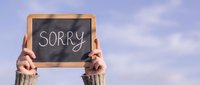 Hands holding a chalkboard with the word Sorry written in chalk against a blue sky, expressing apology, regret, and forgiveness concept.