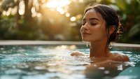 Young Hispanic woman relaxing in swimming pool at sunset with eyes closed, water droplets on face, peaceful expression, golden hour lighting creates serene atmosphere.