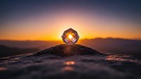 Crystal sphere refracting golden sunset light on wooden surface with mountain silhouettes and dramatic sky creating magical atmospheric scene for meditation concepts.