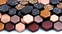 Metallic hexagonal makeup eyeshadow palette with glitter texture in rose gold, copper, burgundy and black shades arranged in honeycomb pattern, close up view.