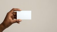 Close-up of a hand with dark skin tone holding a blank white business card against a neutral beige background, suitable for branding and corporate design projects.