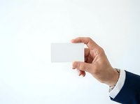 Male hand holding blank white business card against neutral background, suitable for corporate branding and professional mockup designs.