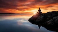 Silhouetted figure meditating on rocky outcrop at sunset over calm lake, reflecting peaceful mindfulness and spiritual wellness practice during golden hour.