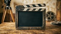 Vintage film clapperboard with blank slate on wooden surface surrounded by filmmaking equipment, ideal for cinema, production, and entertainment industry projects.
