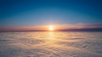 Aerial view of sunrise over endless clouds with golden sunlight breaking through atmospheric layers, suitable for backgrounds and inspirational content.
