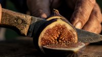 Fresh fig cut in half with knife, showing red interior seeds and flesh, suitable for food photography, culinary content, and healthy eating concepts.