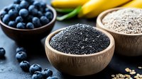 Fresh chia seeds in wooden bowl with blueberries and bananas on dark background, healthy superfood ingredients for breakfast and smoothies.