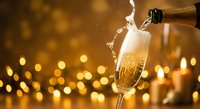 Champagne pouring into flute glass with golden bubbles and foam against warm bokeh lights background for celebration and luxury events.