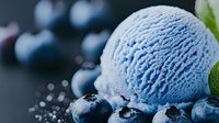 Refreshing blue ice cream scoop with fresh blueberries and mint leaves on dark background, macro shot with selective focus and water drops.