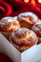 Fresh baked vanilla muffins dusted with powdered sugar in white paper cups and gift box, close up view with soft bokeh lights on red background.