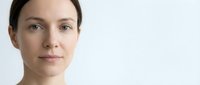 Young Caucasian woman with natural makeup and pulled back hair against clean white background for skincare and beauty concepts.