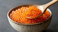 Fresh red caviar in ceramic bowl with wooden spoon, bright orange salmon roe pearls on dark background, close up view of luxury seafood delicacy.