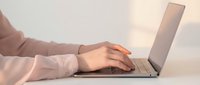 Professional woman hands typing on laptop computer at modern workspace during golden hour lighting for business productivity and remote work.