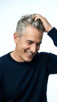 Middle-aged man with gray hair touching head while smiling, wearing dark sweater. Suitable for hair care, aging, confidence, and lifestyle concepts.