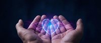 Cupped hands holding glowing translucent heart with blue and purple light effects against dark background for healthcare and love concepts.