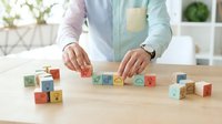 Young adult arranging colorful wooden blocks with letters and numbers on natural wood table, hands visible in casual clothing, educational learning activity for children development.