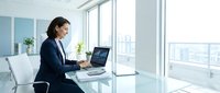 Professional businesswoman working on laptop in modern office with city view through large windows.