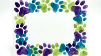 Colorful watercolor paw prints frame border in purple, teal and green hues on white background. Pet care, veterinary clinic, animal lover design element.