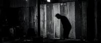 Silhouette of person bending forward in industrial warehouse with corrugated metal walls and dramatic lighting, suitable for noir, mystery, and dramatic storytelling projects.