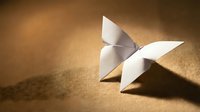 White origami butterfly resting on warm golden textured surface, casting soft shadow, symbolizing creativity, transformation, and mindfulness in art.