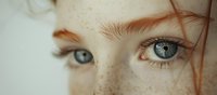 Close up view of bright blue eyes and natural freckles on fair skin with ginger eyebrows, capturing innocence and natural beauty in soft lighting.