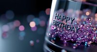 Sparkling purple glitter and happy birthday text in glass container against blurred bokeh background creates festive celebration atmosphere.
