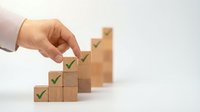 Hand placing wooden blocks with green checkmarks in ascending steps representing business growth, success milestones, and achievement progress concept.