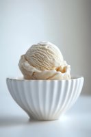 Creamy vanilla ice cream scoop served in elegant white fluted ceramic bowl against light background, minimalist food photography composition for dessert menus.