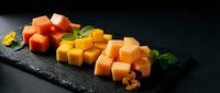 Assorted aged cheese cubes with nuts and fresh herbs arranged on dark slate board for gourmet appetizer and wine pairing presentations.