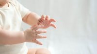 Baby hands reaching out in soft natural light on white background for parenting and childcare concepts.