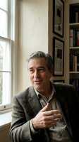 Mature Caucasian businessman in gray suit gesturing while speaking in home office with bookshelves and natural window light for professional consultation.