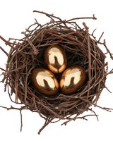 Three golden eggs nestled in brown twig nest against white background, symbolizing wealth, investment and financial security. Isolated object for design use.