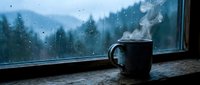 Steaming mug on a rustic wooden windowsill with rain-streaked glass and misty forest in the background, evoking cozy autumn comfort.