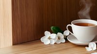 Steaming cup of hot tea with delicate white apple blossom flowers on wooden table surface, creating serene morning atmosphere for wellness and relaxation.