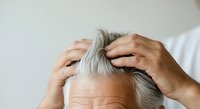 Senior man with gray hair examining receding hairline and hair loss on white background, suitable for healthcare, dermatology, and wellness content.