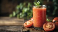 Fresh tomato juice in glass with mint garnish on rustic wooden table surrounded by ripe tomatoes and herbs for healthy organic beverage concept.