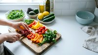 Hands chopping fresh colorful vegetables on wooden cutting board in modern kitchen for healthy meal preparation and cooking.