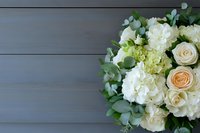 Elegant bouquet of white hydrangeas, cream roses, and eucalyptus leaves arranged on gray wooden background, ideal for wedding or event decoration.