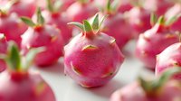 Fresh dragon fruit with bright pink skin and green leaves arranged in rows on white surface, macro food photography showing vibrant tropical produce texture.
