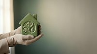 Hands holding green eco-friendly house model with leaf and water drop symbols representing sustainable living and environmental conservation concept.