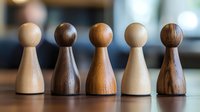 Five wooden pawn figures in different wood tones standing in row on table surface representing teamwork diversity leadership and business concepts.