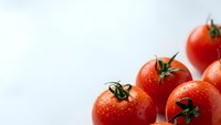Fresh red ripe tomatoes with green stems and water droplets on white background for healthy cooking and organic food concepts.