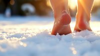 Bare feet walking in fresh powder snow at sunset with magical golden bokeh lights, creating peaceful winter atmosphere for wellness and nature concepts.